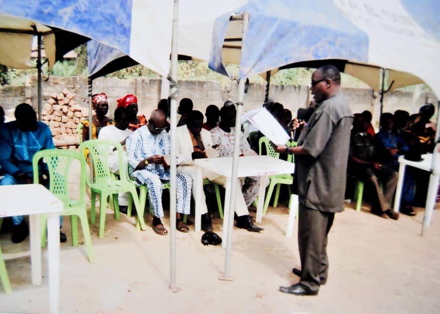 Speaker addresses people seated under a tent at a community gathering