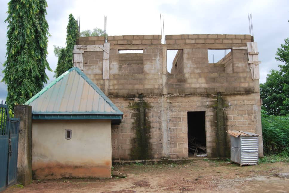 An unfinished concrete building beside a small gatehouse